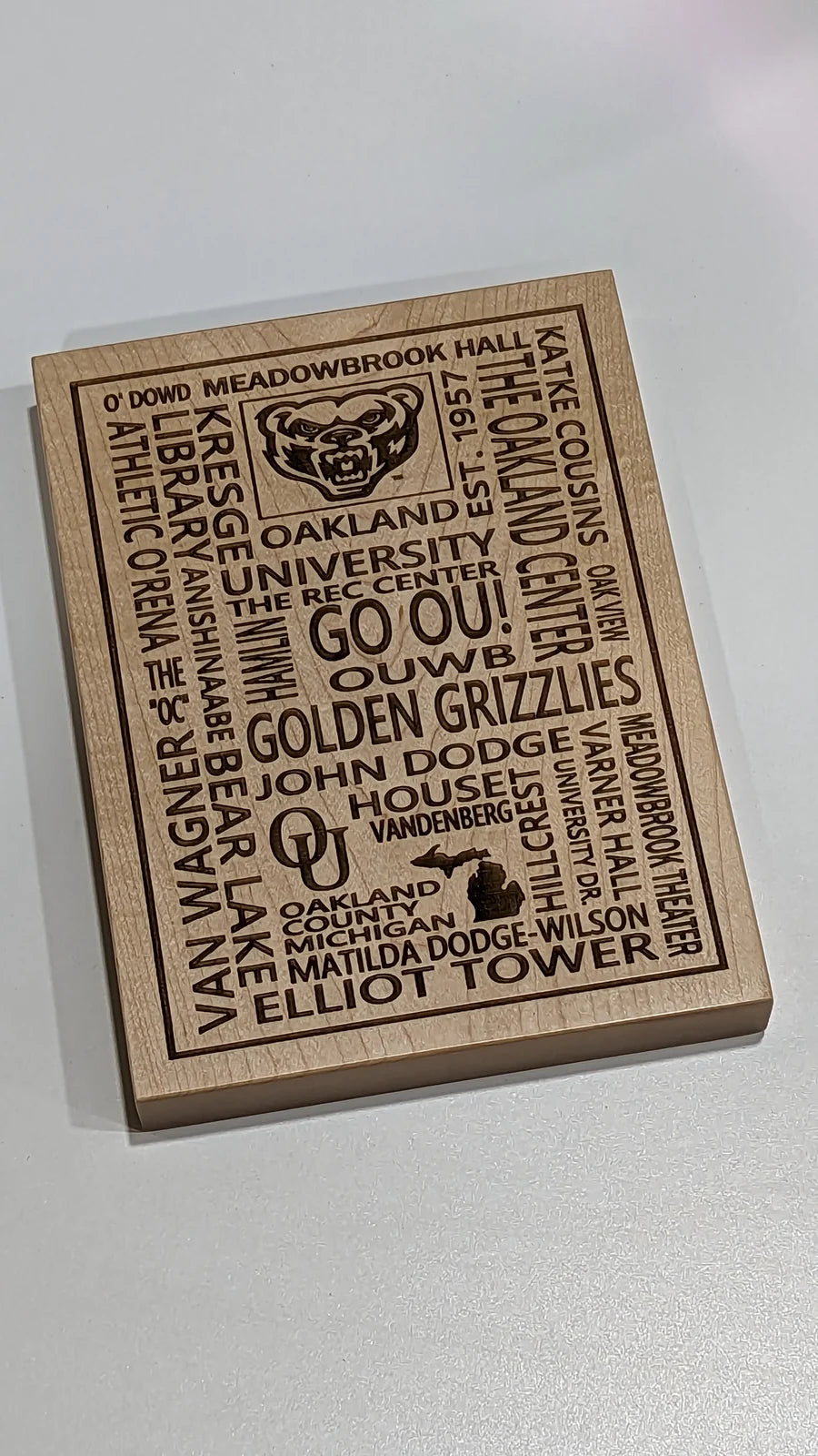 A maple word plaque listing Oakland University landmarks and traditions.