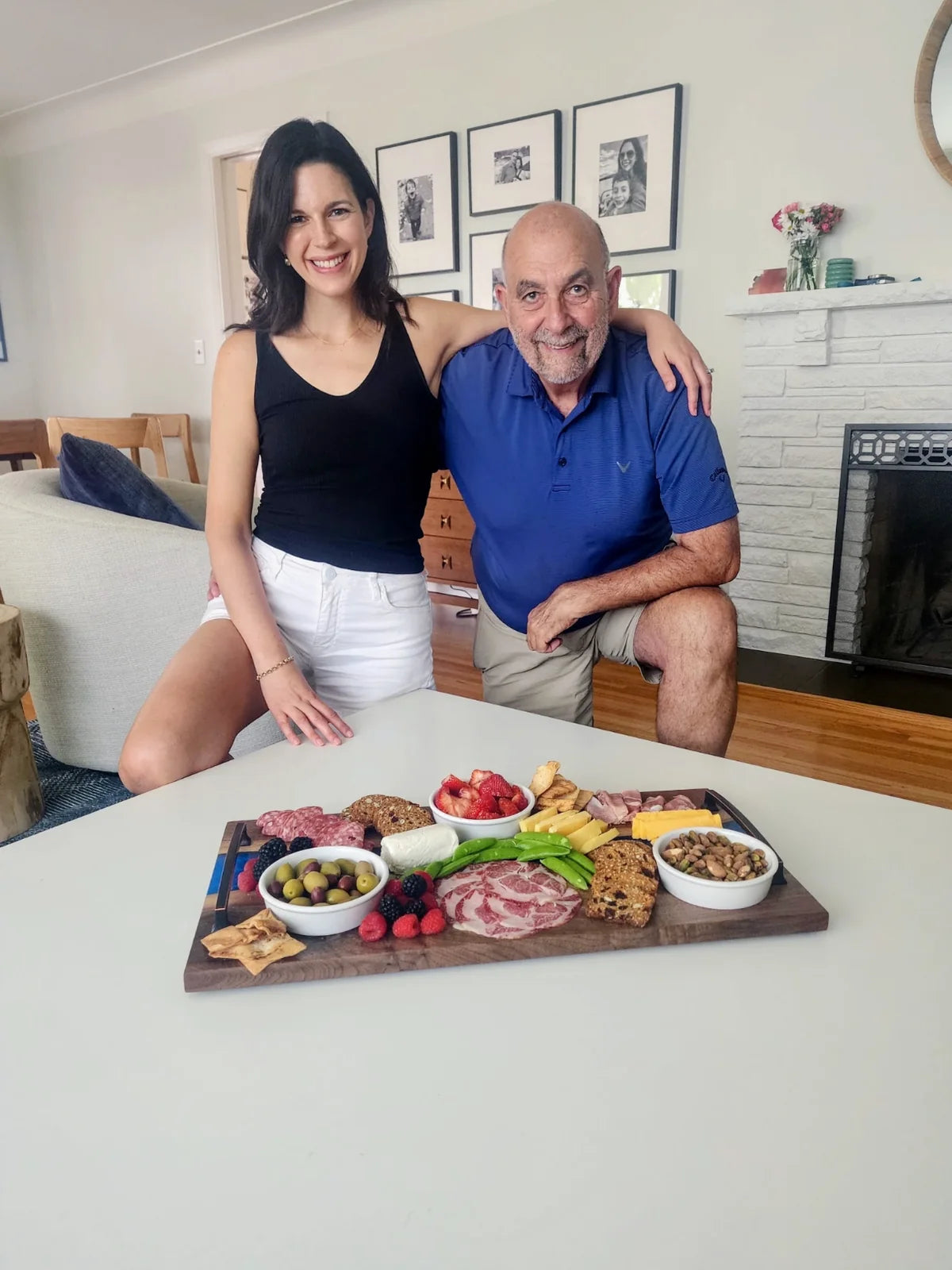 Valerie Mastroianna and Jim behind the walnut and aqua resin charcuterie board, spread with meats, cheeses and fruit.